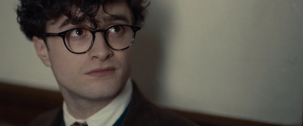 Kill Your Darlings (2013) movie still: closeup — A man stands indoors against a plain light-colored wall. He turns his head to look toward the right…