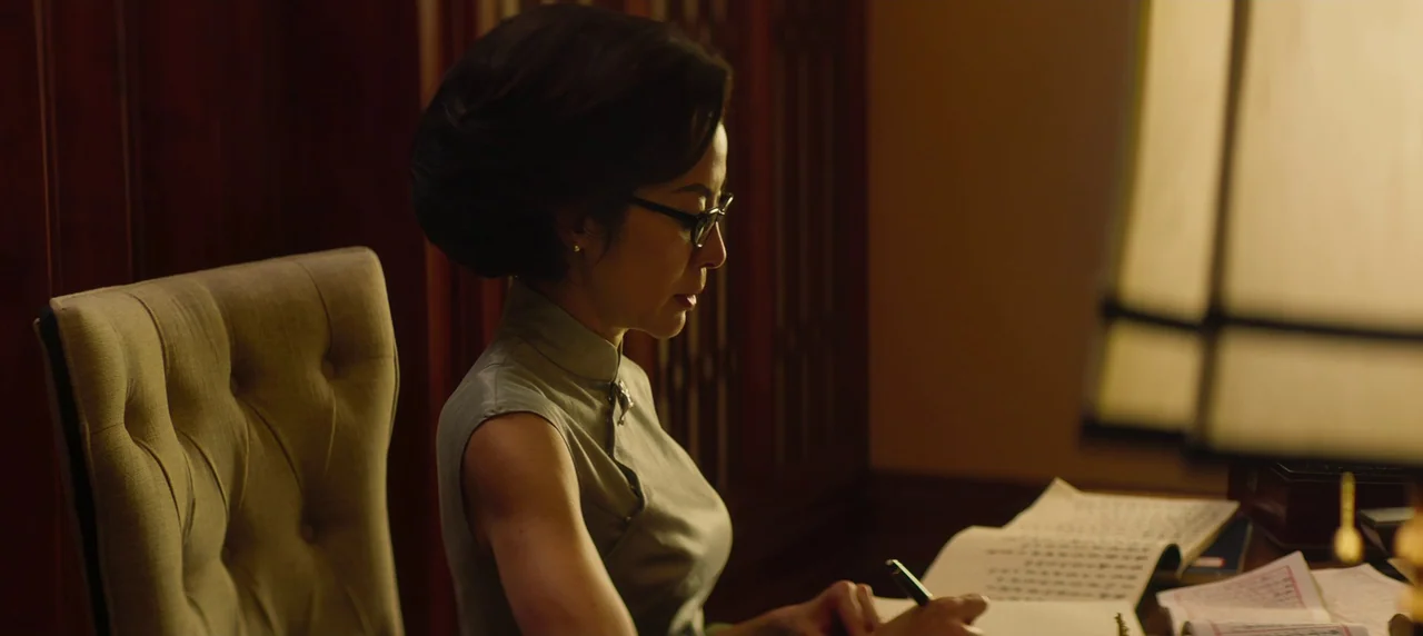 Master Z: The Ip Man Legacy (2018) movie still: medium — A wooden paneled room contains a desk and a tufted fabric chair. A woman sits in the chair…