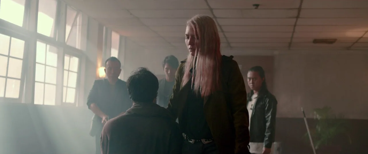 The Night Comes for Us (2018) movie still: medium — An interior space with a dropped ceiling and dusty air illuminated by side windows. A group of…
