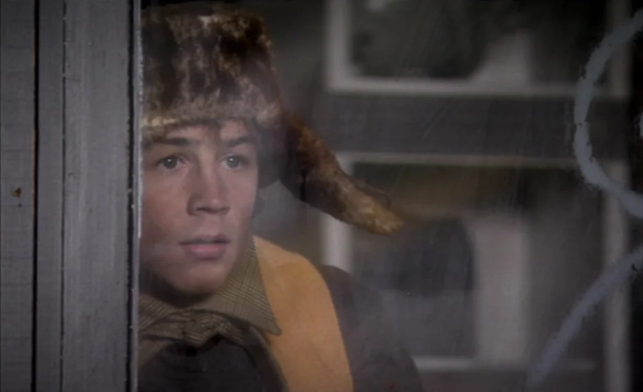 Dear Wendy (2005) movie still: closeup — A person looks through a glass window pane from a dimly lit interior. The focus is tightly cropped on the…