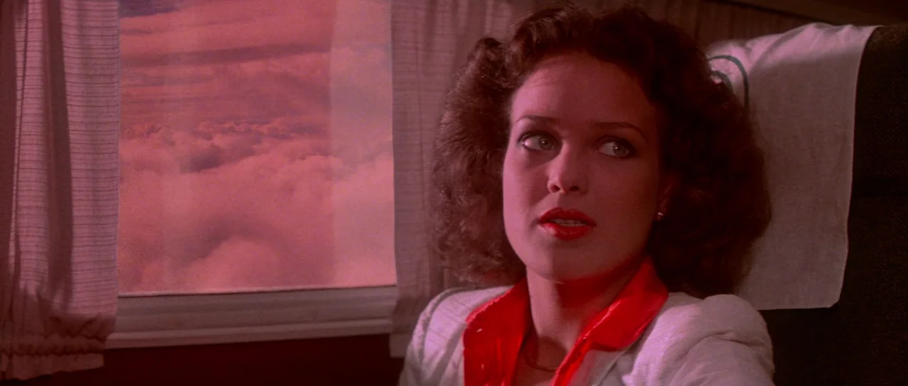 Flash Gordon (1980) movie still: closeup — The interior of an airplane cabin features fabric curtains and a view of clouds. A woman sits in her seat…