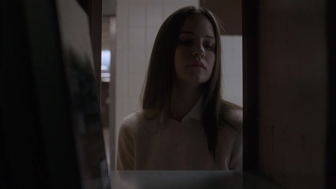 The Babysitters (2008) movie still: medium — A teenager stands in front of a metal locker in a tiled hallway. The student looks down into the…