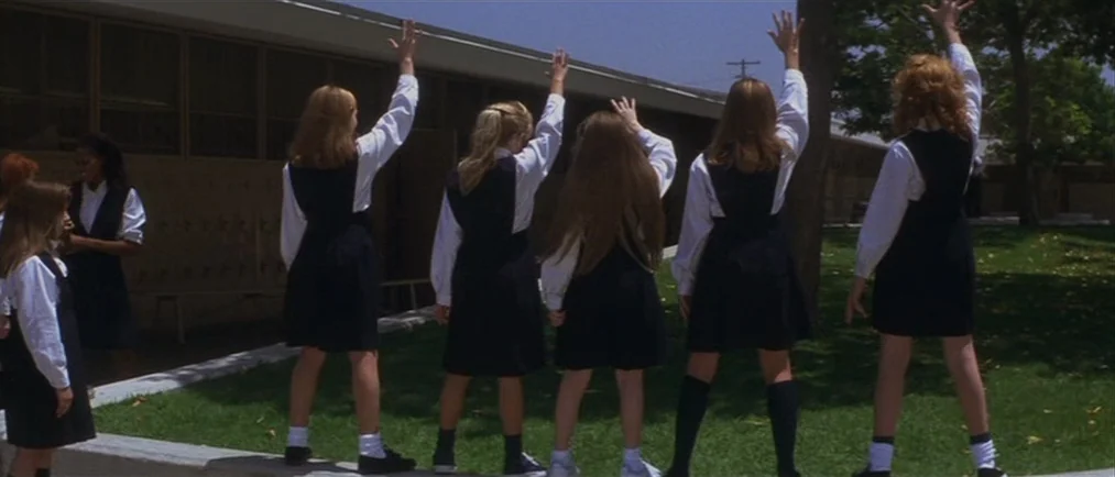 Donnie Darko movie still: wide — A row of schoolgirls in uniforms stands outside a single-story brick school building. They are lined up on a grassy…