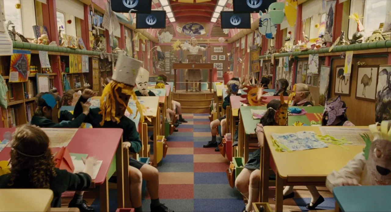 Snowpiercer (2013) movie still: wide — A train car interior converted into a primary school classroom filled with student desks. Children wearing…