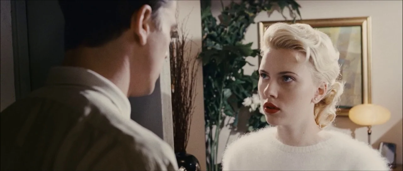 The Black Dahlia (2006) movie still: medium — An interior space features a blonde woman looking toward an out-of-focus man. A decorative painting…
