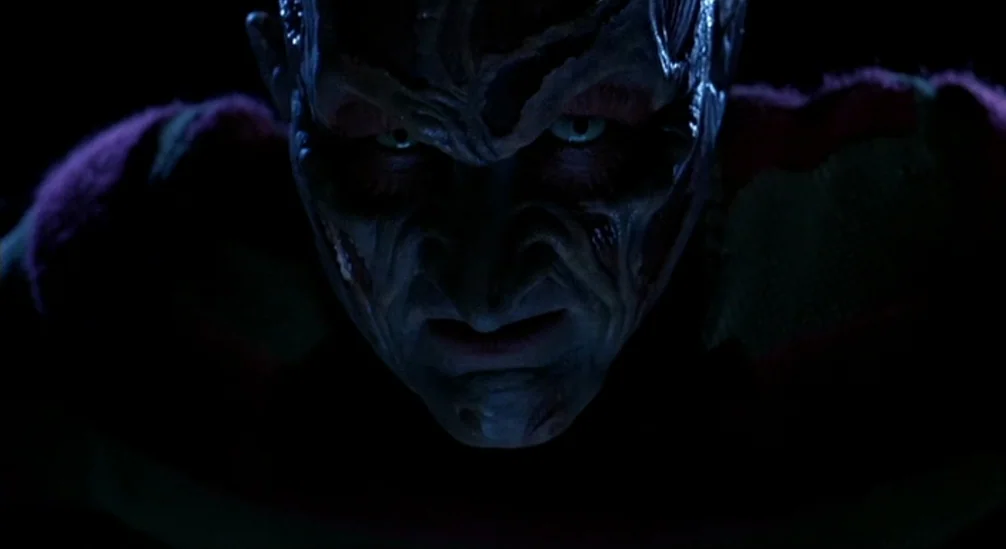 New Nightmare (1994) movie still: closeup — A man with heavily scarred, burnt facial skin stares forward in a dark environment. The figure occupies…