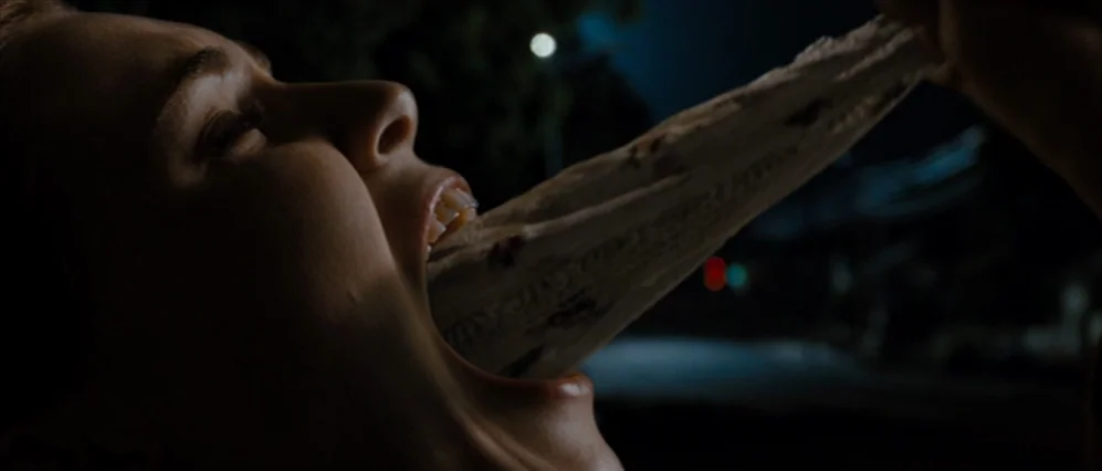 Drag Me to Hell (2009) movie still: closeup — A close up shows the side profile of a woman at night. She pulls a long piece of partially eaten food…