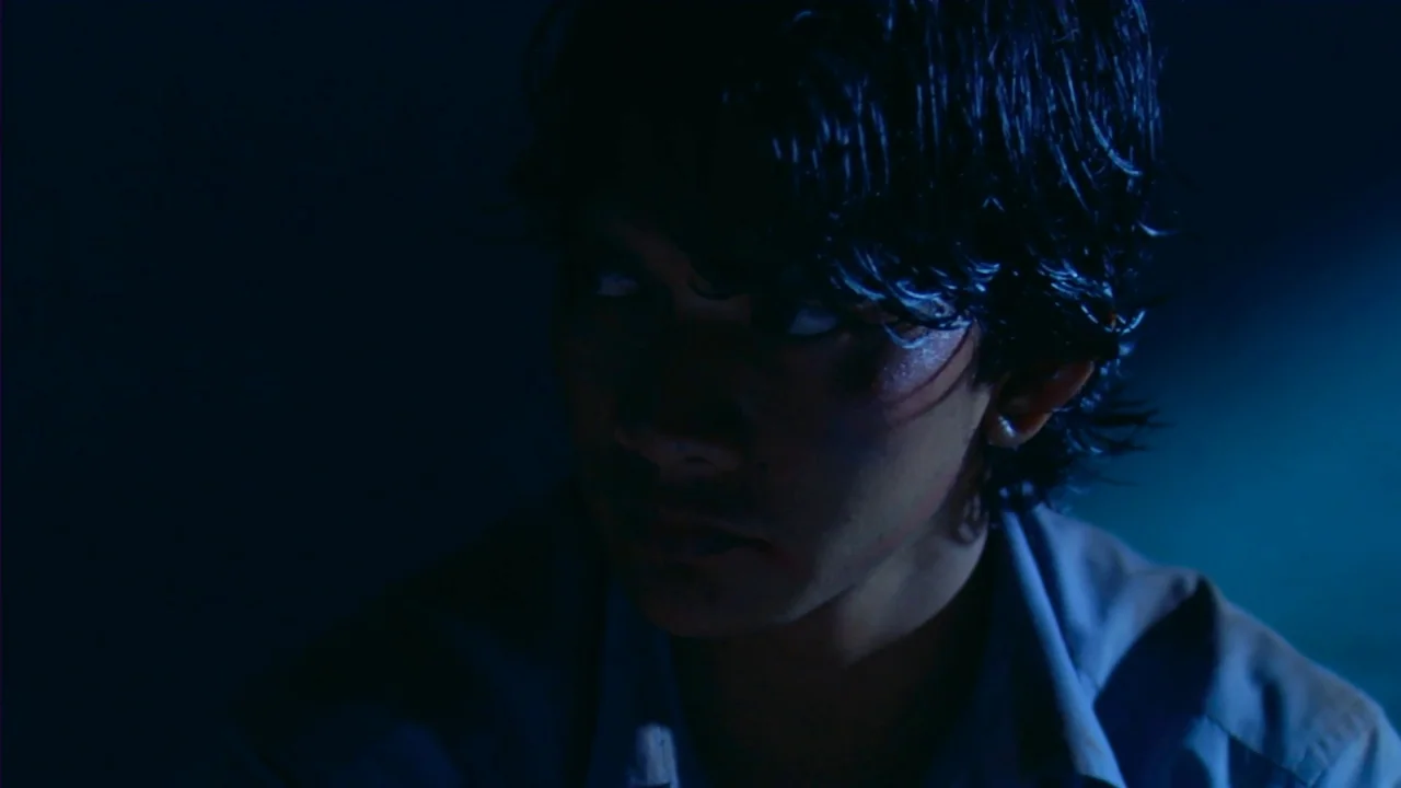 Merantau (2009) movie still: closeup — A dark, dimly lit room is illuminated only by a cool blue light source. A young man with dark, damp hair…