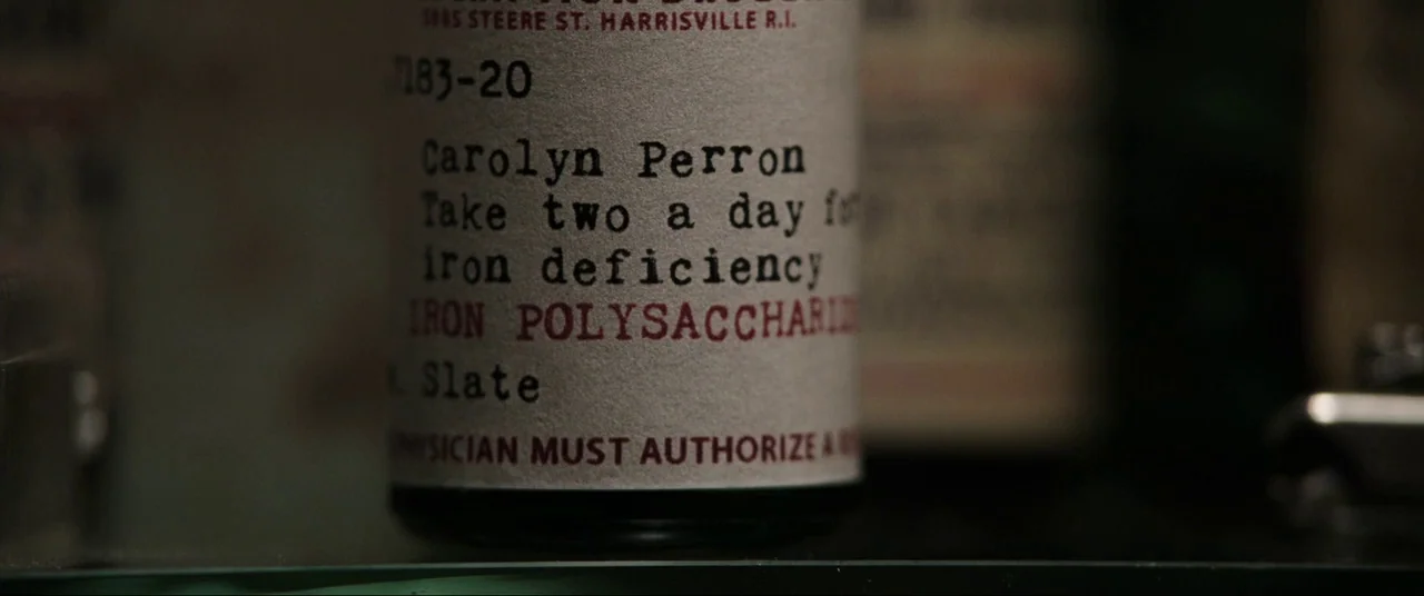 The Conjuring (2013) movie still: closeup — A close-up shot of a white medicine bottle label with typed instructions in black ink. The label…