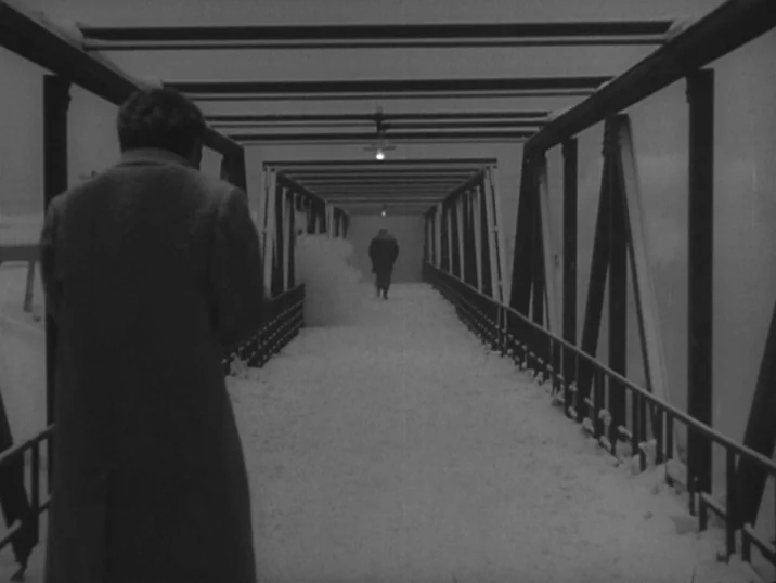 The Idiot (1951) movie still: medium — A snow-covered metal pedestrian bridge stretches into the darkness of a winter night. One man walks away in…
