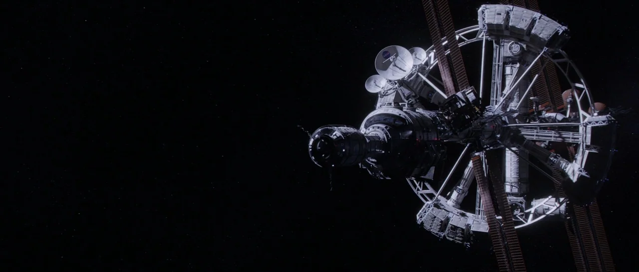 The Martian (2015) movie still: establishing — A complex, rotating space station orbits in the vast darkness of deep space. White solar panels,…