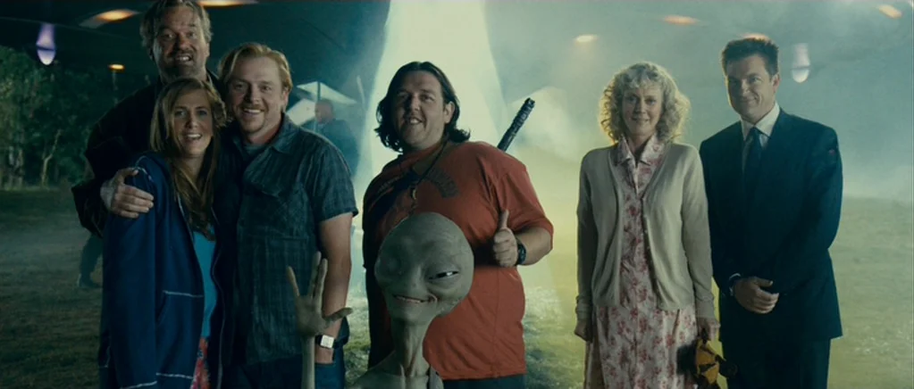 Paul (2011) movie still: fullbody — An open field with a large metallic craft partially visible in the sky. A diverse group of people stand beside a…