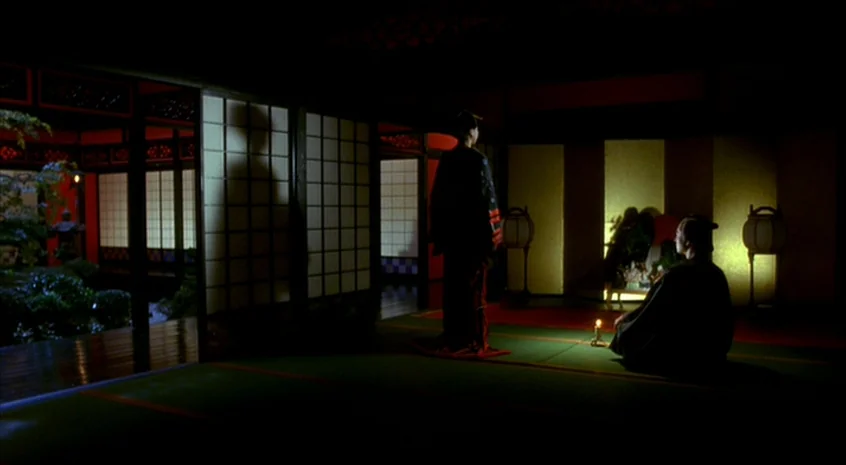Sakuran (2006) movie still: wide — A dark, traditional Japanese room with tatami flooring and glowing shoji paper panels. Two figures sit and stand…