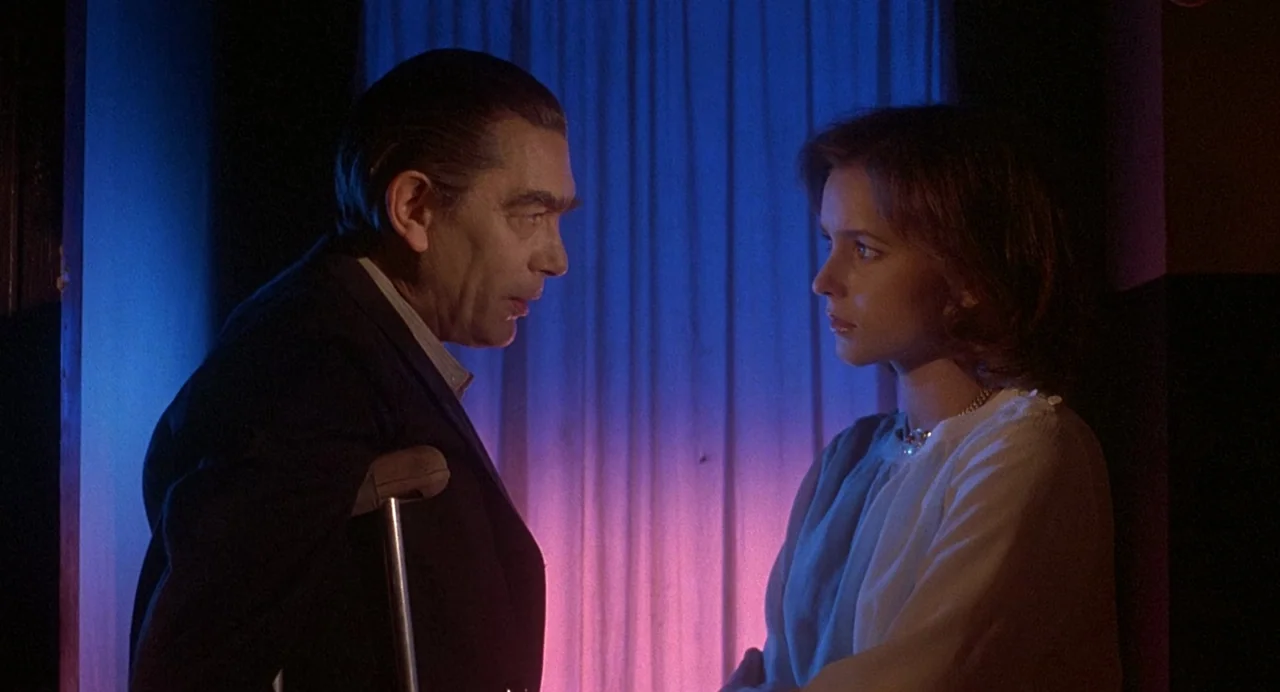 Inferno (1980) movie still: medium — An interior space is illuminated by vibrant neon blue and pink light sources. A man with a crutch confronts a…