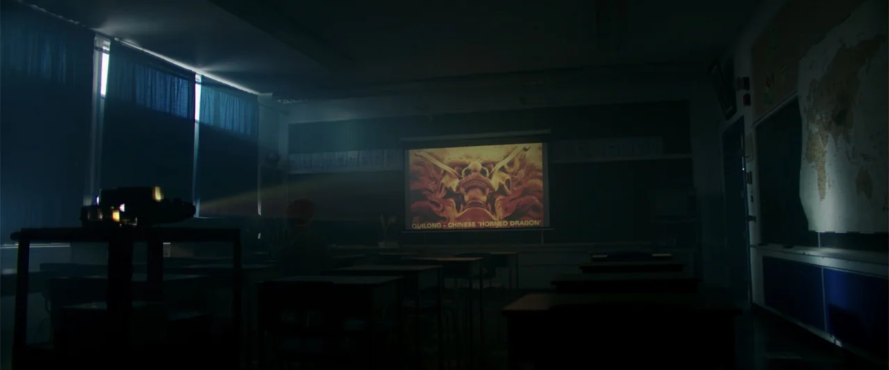 K.G.F: Chapter 2 (2022) movie still: wide — A dimly lit classroom features rows of desks and a wall-mounted world map. A red-haired student sits at…