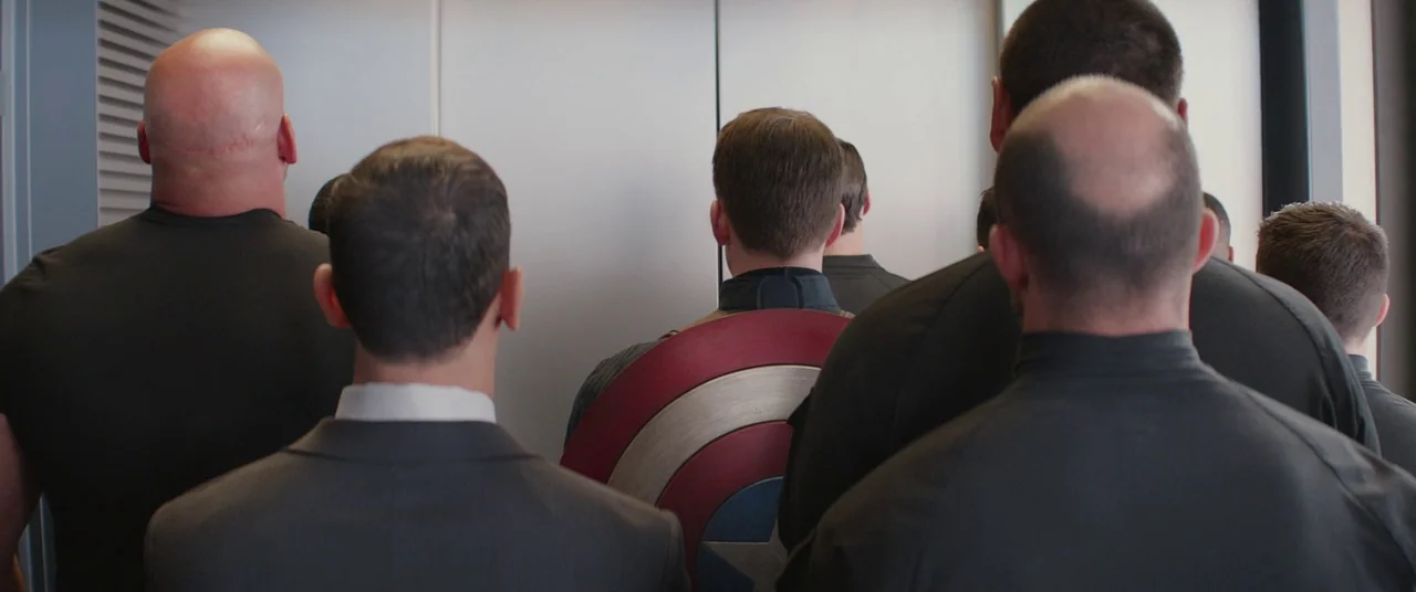 Captain America: The Winter Soldier (2014) movie still: medium — A group of men stand within a cramped, metallic elevator with closed silver doors.…