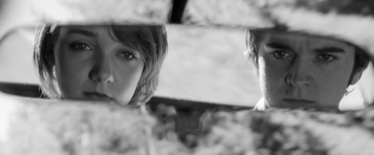 Weirdos (2016) movie still: closeup — A close-up shot captured in a car's rearview mirror showing two people. The man and woman look directly into…