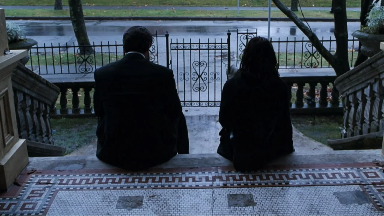 Get Carter (2000) movie still: medium — A residential building entrance with tiled steps and a decorative iron fence. Two people sit quietly on the…