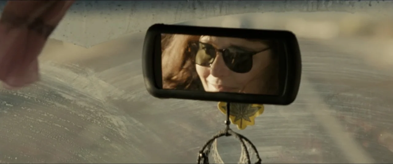 Into the Wild (2007) movie still: closeup — The interior of a vehicle displays a dusty windshield and a rearview mirror. A woman's face is clearly…