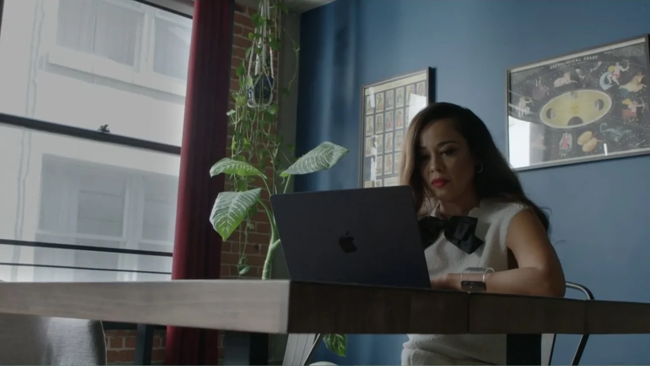 Chris Brown: A History of Violence (2024) movie still: medium — A home office features a blue wall, exposed brick, and a large window. A woman sits…