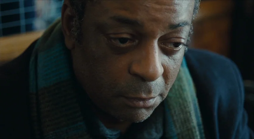 35 Shots of Rum (2008) movie still: closeup — A man sits inside a booth with a dark wood background and grid pattern. He is looking down at a…