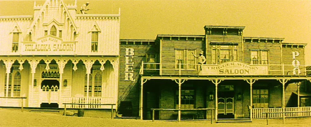 Lemonade Joe (1964) movie still: wide — A pair of wooden nineteenth-century saloon buildings stand side by side on a dusty street. The buildings…