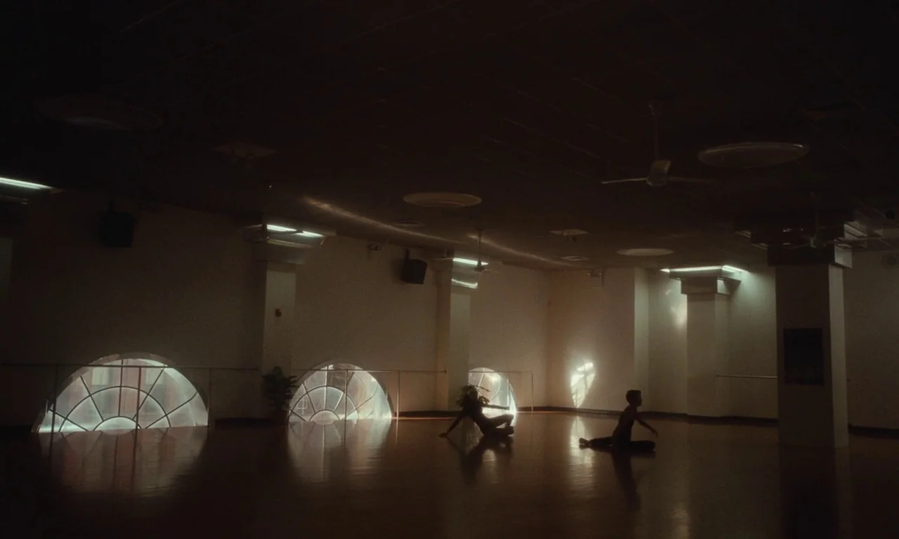 Vox Lux (2018) movie still: wide — A spacious dance rehearsal room features hardwood flooring and multiple low semi-circular windows. Two dancers…