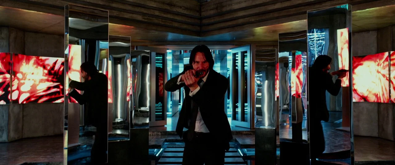 John Wick: Chapter 2 (2017) movie still: medium — A dark gallery space filled with vertical mirrors and bright red illuminated display panels. A man…