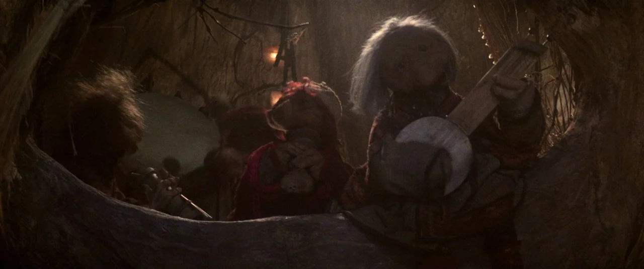 The Dark Crystal (1982) movie still: medium — A group of puppets plays instruments inside a darkened, weathered hollow tree interior. The puppets…