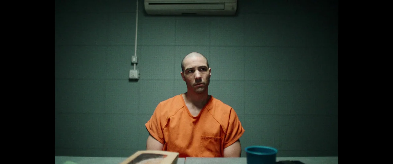 The Mauritanian (2021) movie still: medium — An interrogation room features dark teal tiled walls and an air conditioning unit. A bald man wearing…