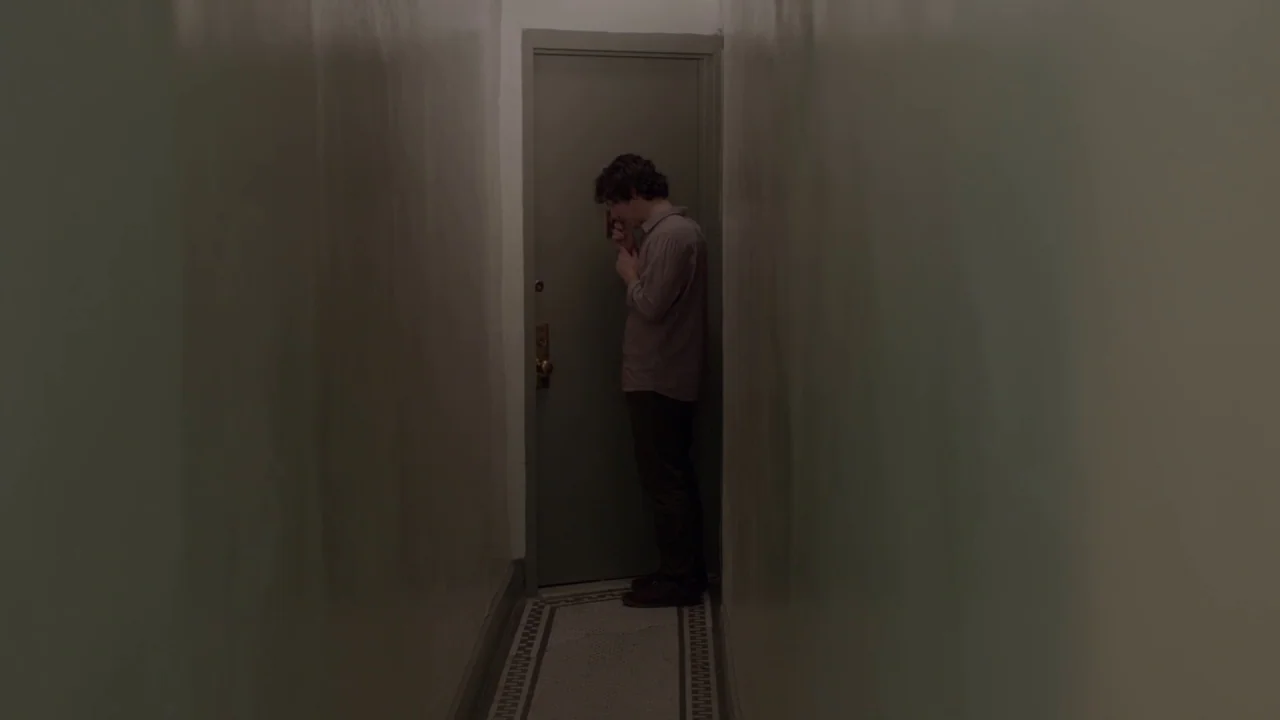 The Heart Machine (2014) movie still: fullbody — A narrow residential hallway features painted walls and a classic tiled floor pattern. A man stands…