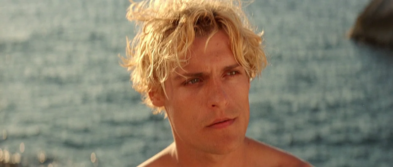 Arabian Nights: Volume 3 The Enchanted One (2015) movie still: closeup — A man stands outdoors near a body of water during late afternoon. The…