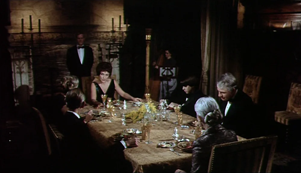 Harold and Maude (1971) movie still: wide — A dark, wood-paneled room features a long table covered in a gold lace cloth. Several people in formal…