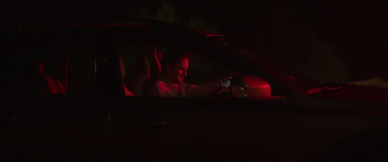 Pet Sematary (2019) movie still: medium — A man sits inside a dark vehicle at night surrounded by total blackness. The interior is bathed in an…