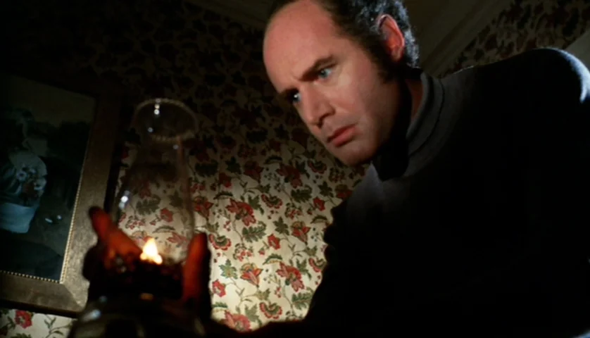 Let’s Scare Jessica To Death (1971) movie still: medium — A dark corridor features floral wallpaper and a framed portrait on the wall. A man in a…