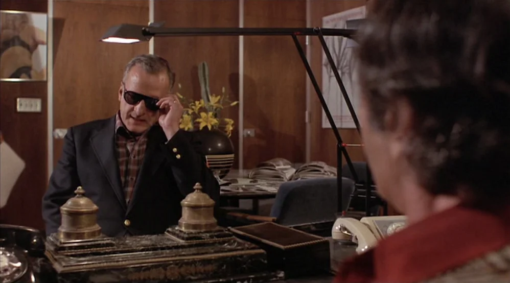 Hardcore (1979) movie still: medium — A wood-paneled office environment features an ornate desk set with inkwells and papers. A middle-aged man in a…