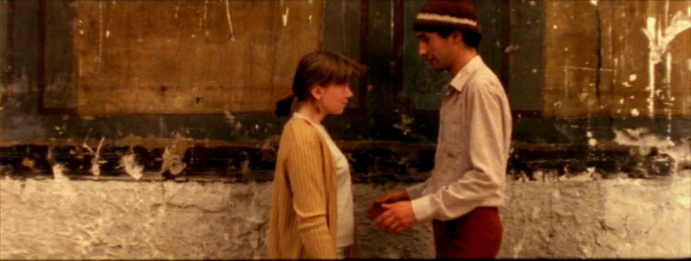 Carne (1991) movie still: medium — A pair of teenagers stand before a wall with worn plaster and paint texture. They face one another in an alley,…