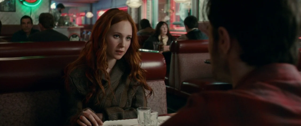 Horns (2013) movie still: medium — A dark diner booth features deep red vinyl seats and tables with clear glasses. A woman with long red hair sits…