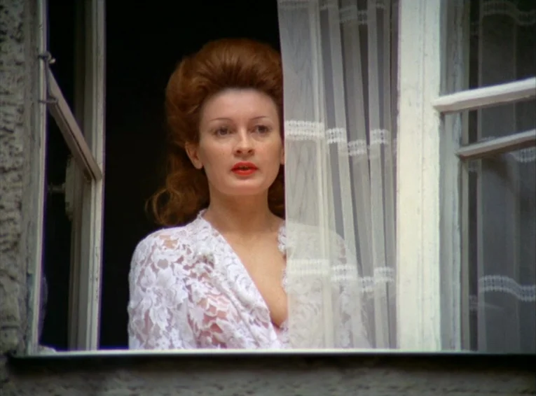 The Merchant Of The Four Seasons (1971) movie still: medium — A woman stands behind an open window framed by sheer white curtains. She looks ahead…