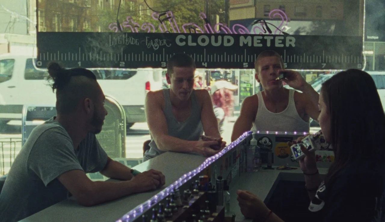 Beach Rats (2017) movie still: medium — A bright storefront interior features a long counter with vaping supplies and neon lights. Four young adults…