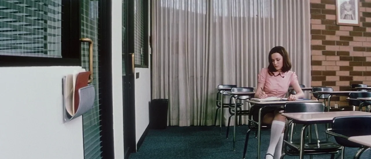 Pretty Persuasion (2005) movie still: wide — A school room with a brick wall, beige floor-to-ceiling curtains, and rows of desks. A teenage girl…