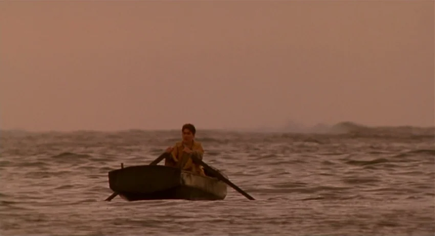 The Secret Of Roan Inish (1994) movie still: wide — A small wooden rowboat sits in the middle of a vast, calm ocean. A young man sits in the center…