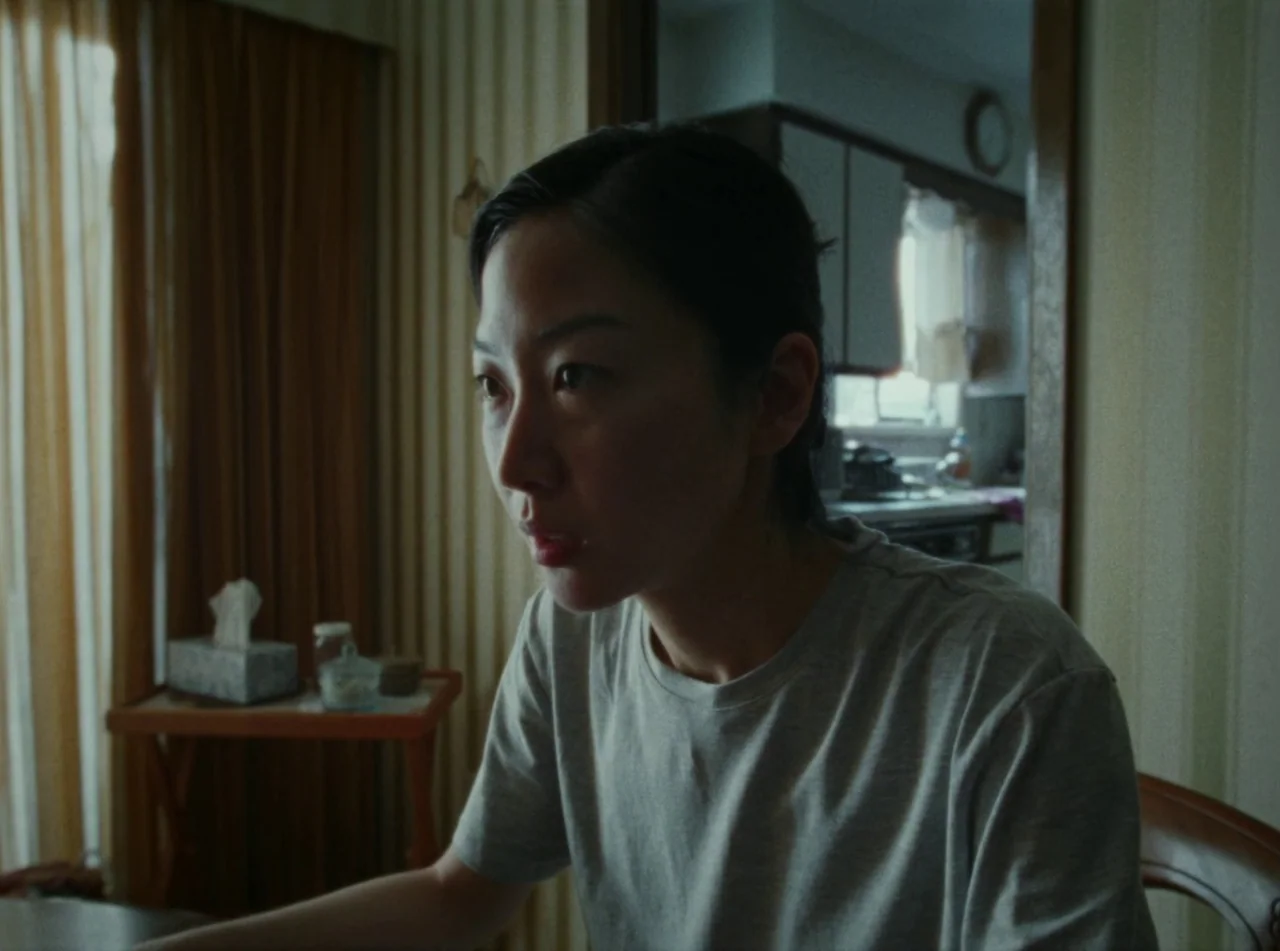 Riceboy Sleeps (2022) movie still: medium — A residential room features vertical-striped wallpaper and a wood-framed doorway leading into a kitchen.…