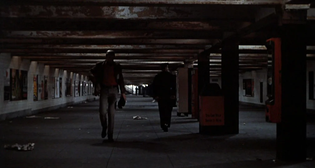 Midnight Cowboy (1969) movie still: wide — A long, dimly lit subway underpass features rows of tiled walls and support pillars. A man walks toward…