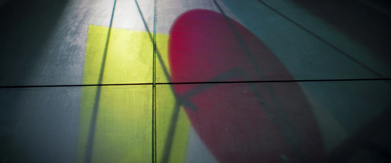 Inside (2023) (2023) movie still: establishing — A clean, smooth floor with panel seams is illuminated by overlapping colored light beams. Large…