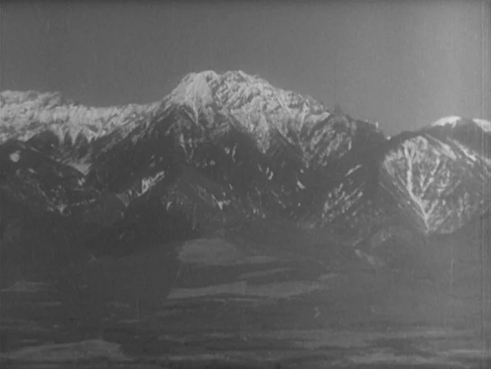 Scandal (1950) movie still: establishing — A vast, snow-capped mountain range rises above a darkened, flat valley floor. The peaks show sharp ridges…