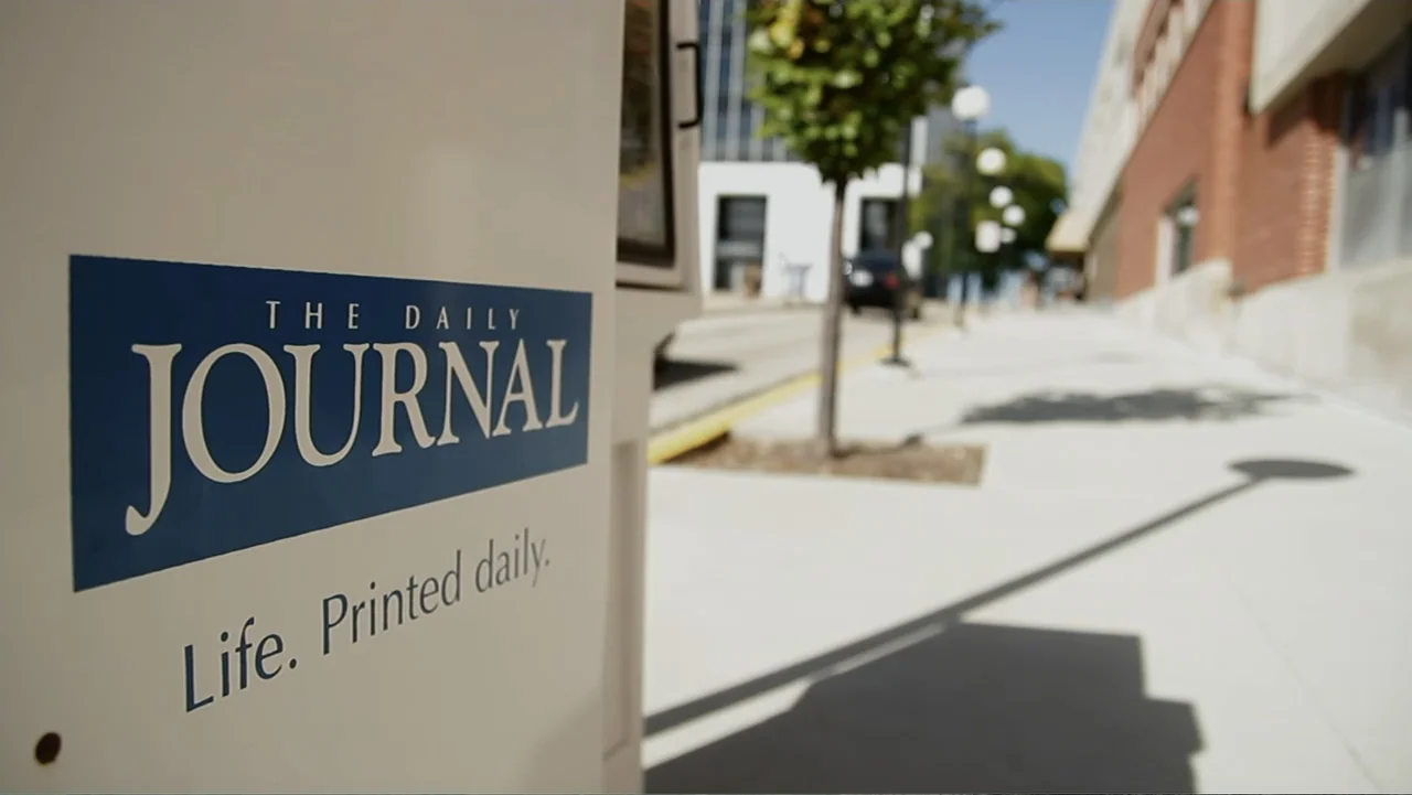 Control (2022) movie still: closeup — A white newspaper vending machine features a dark blue logo on its side panel. The machine occupies the…
