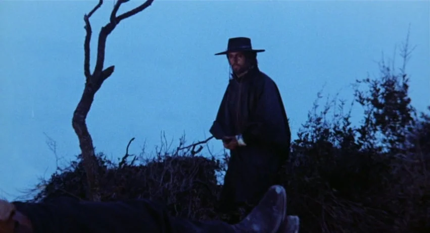Roy Colt and Winchester Jack (1970) movie still: medium — An open rural landscape at twilight features a dead tree and low brush. A man in a western…
