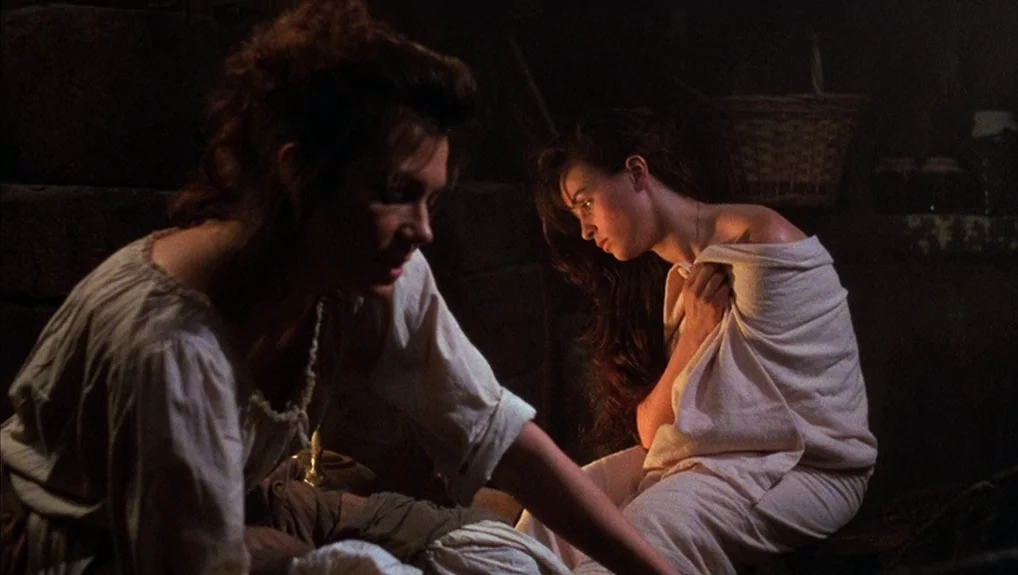 The Company of Wolves (1984) movie still: medium — A dark subterranean space features stone walls and a woven basket in the background. Two women…