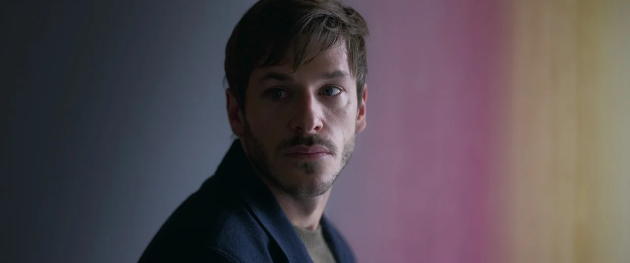 More Than Ever (2022) movie still: closeup — A dimly lit indoor space features a wall with a soft vertical color gradient. A man stands in the…
